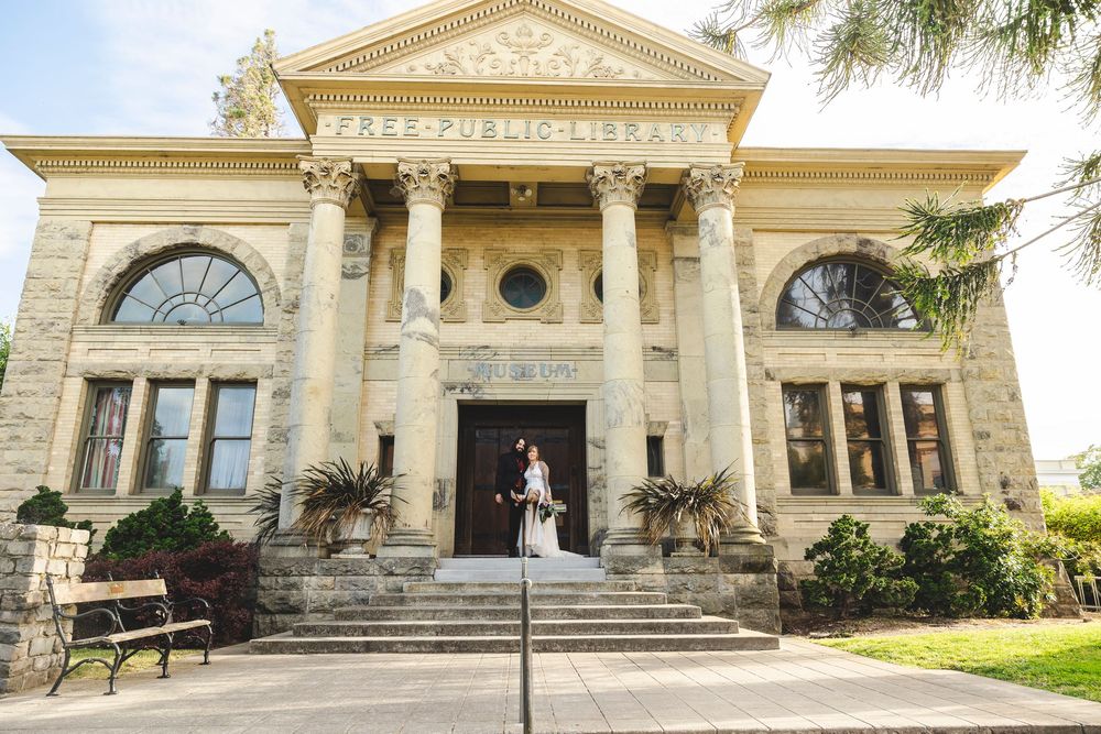 Bride and groom pose on steps of historic Free Public Library building with stone columns.