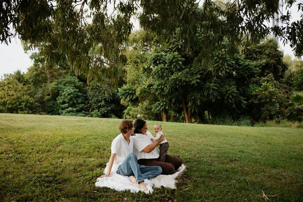 Couple sitting on a blanket in a lush green park, sharing a relaxed outdoor picnic moment together.