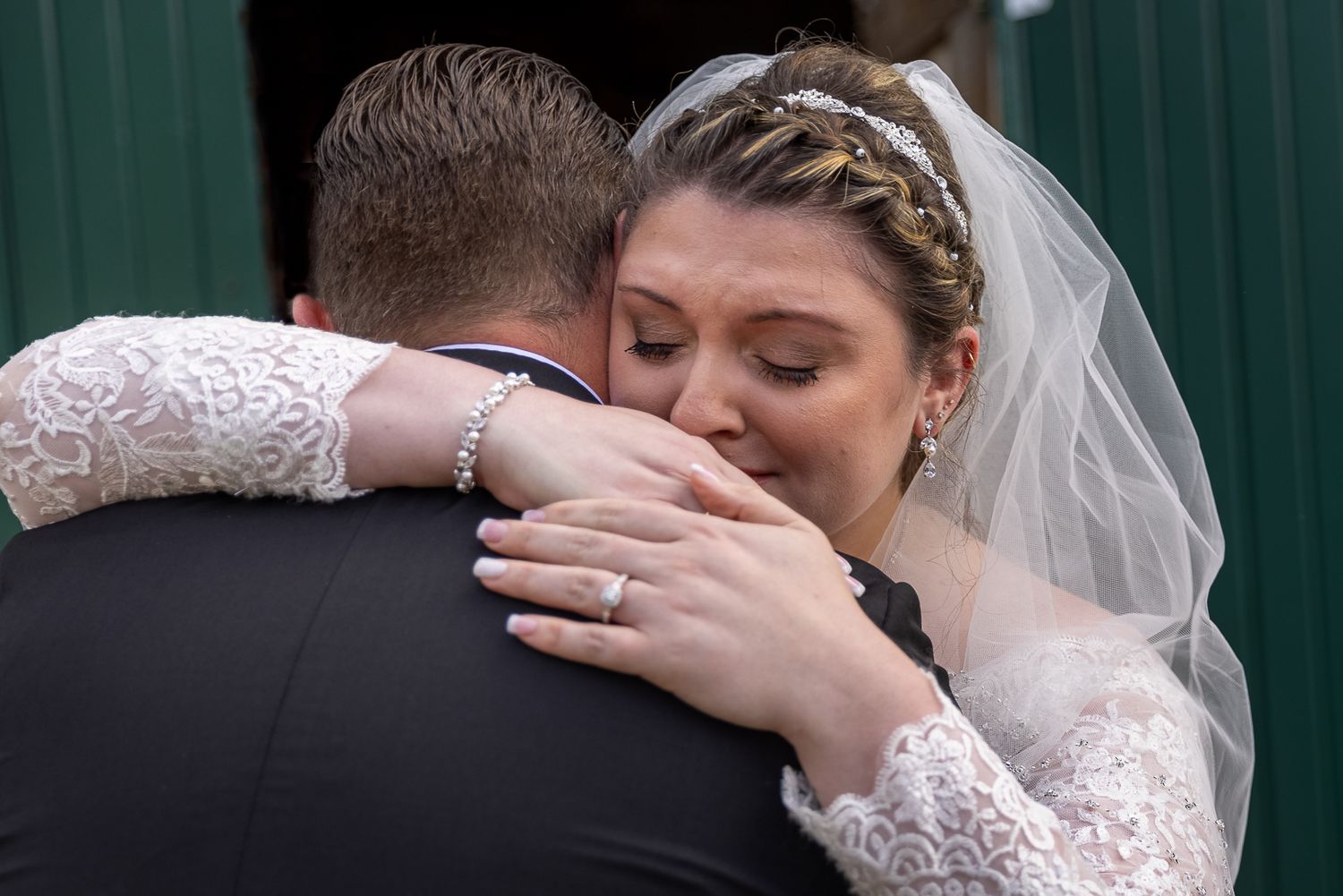 Emotional bride in lace gown and veil embracing groom during wedding ceremony, showing heartfelt moment.