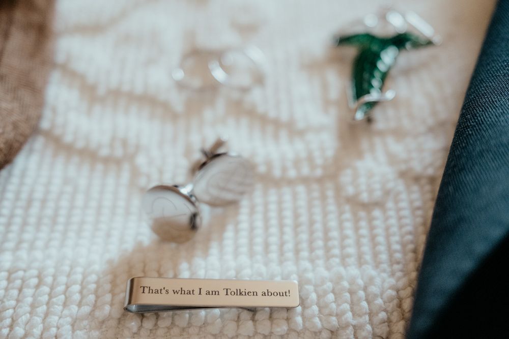 Close-up of wedding cufflinks and a humorous Tolkien quote tie clip on a textured white suit lapel.