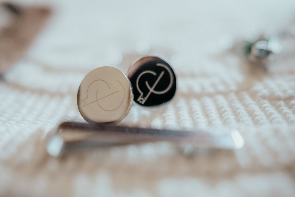 Two elegant cufflinks with engraved monogram initials, one gold and one black, resting on a textured white surface.