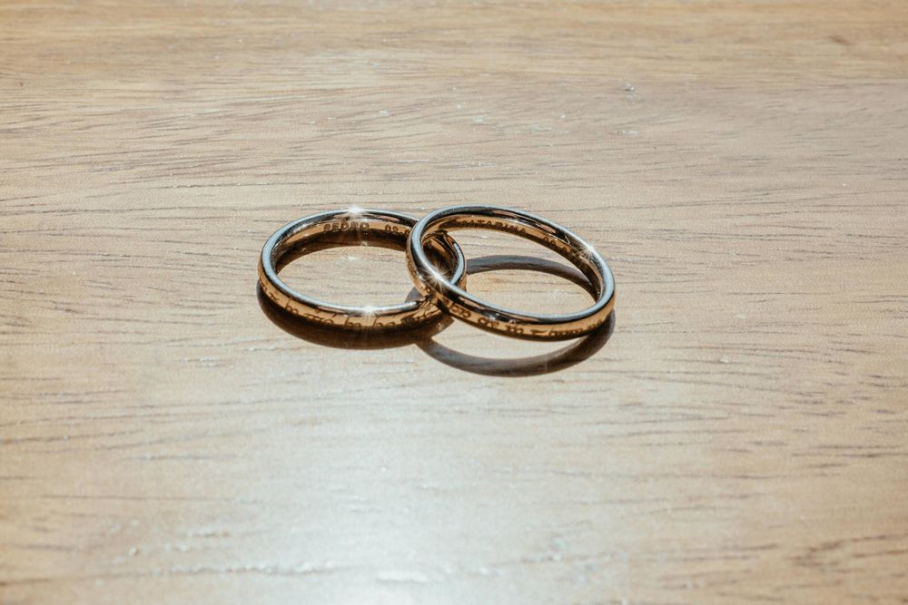 Two interlocked gold wedding bands resting on a light wooden surface, symbolizing love and commitment.