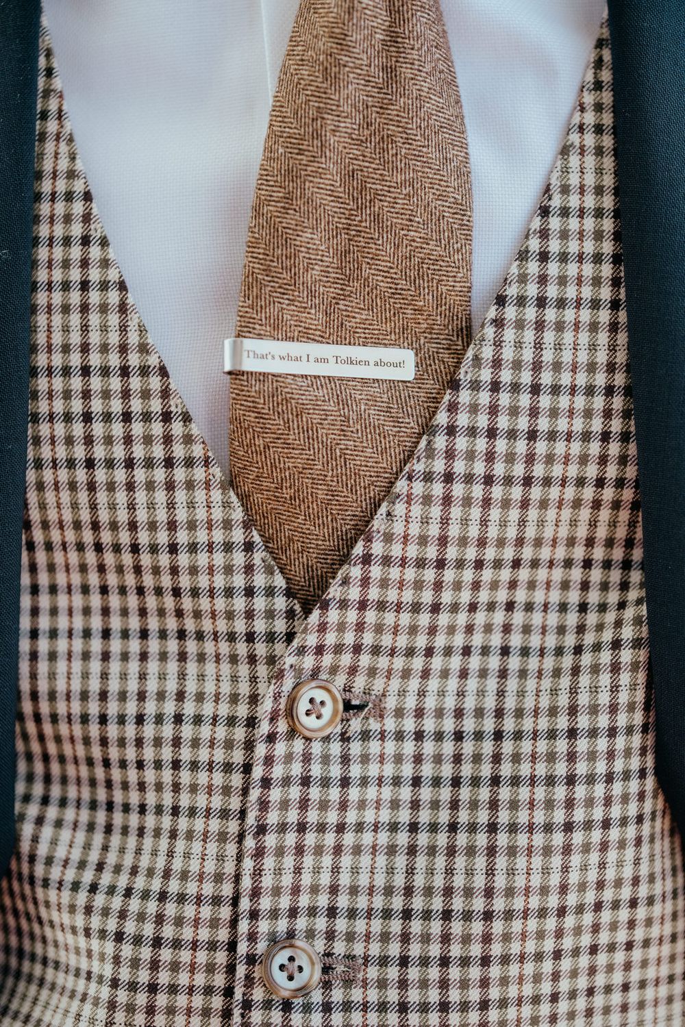 Groom's tweed vest and herringbone tie with a Tolkien-themed tie bar, perfect for a Lord of the Rings wedding.