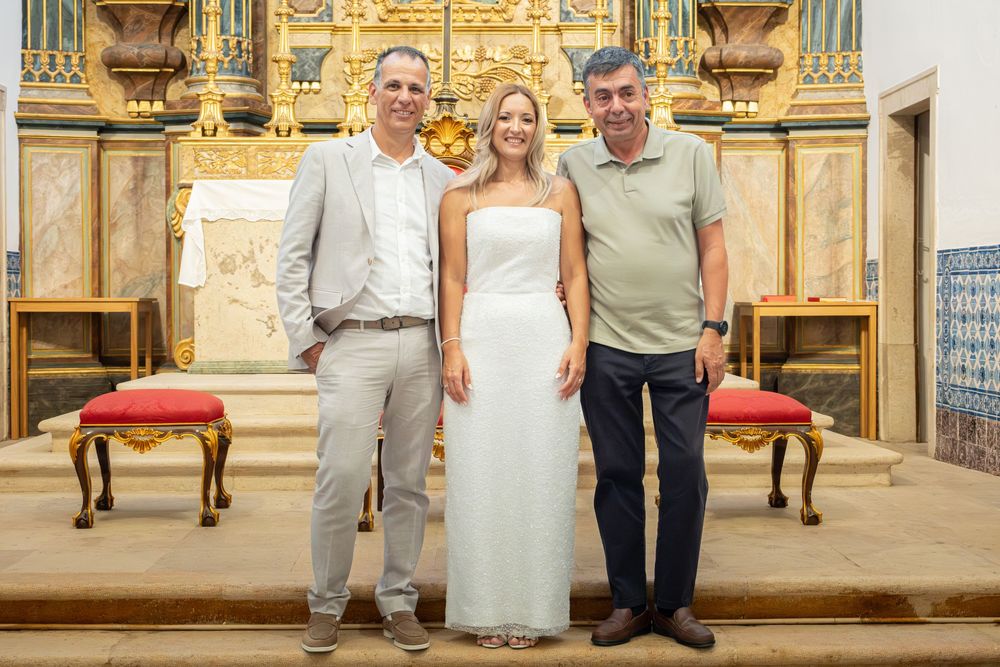 Two men and a woman in a white dress pose together inside an ornate church with a golden altar backdrop.