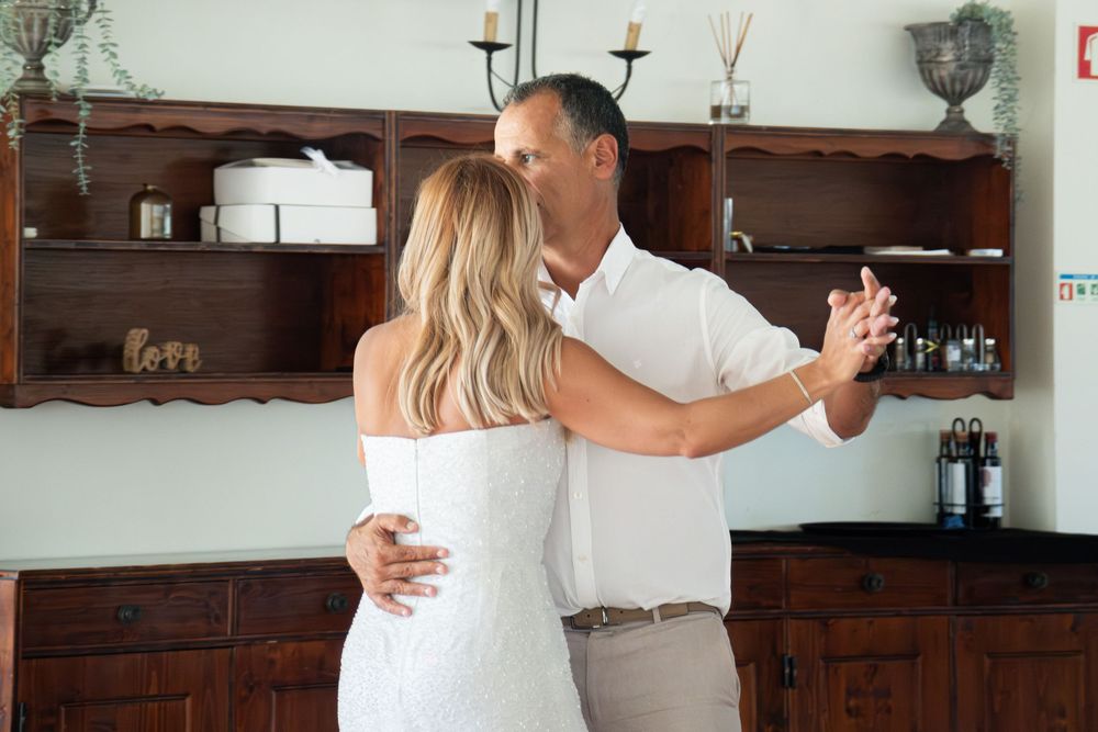 Couple sharing a romantic first dance in white wedding attire inside a rustic wooden interior.