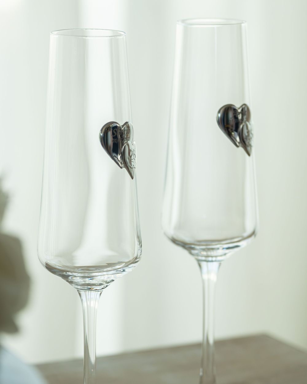 Two elegant crystal champagne flutes featuring decorative silver heart charms, perfect for weddings or romantic celebrations.