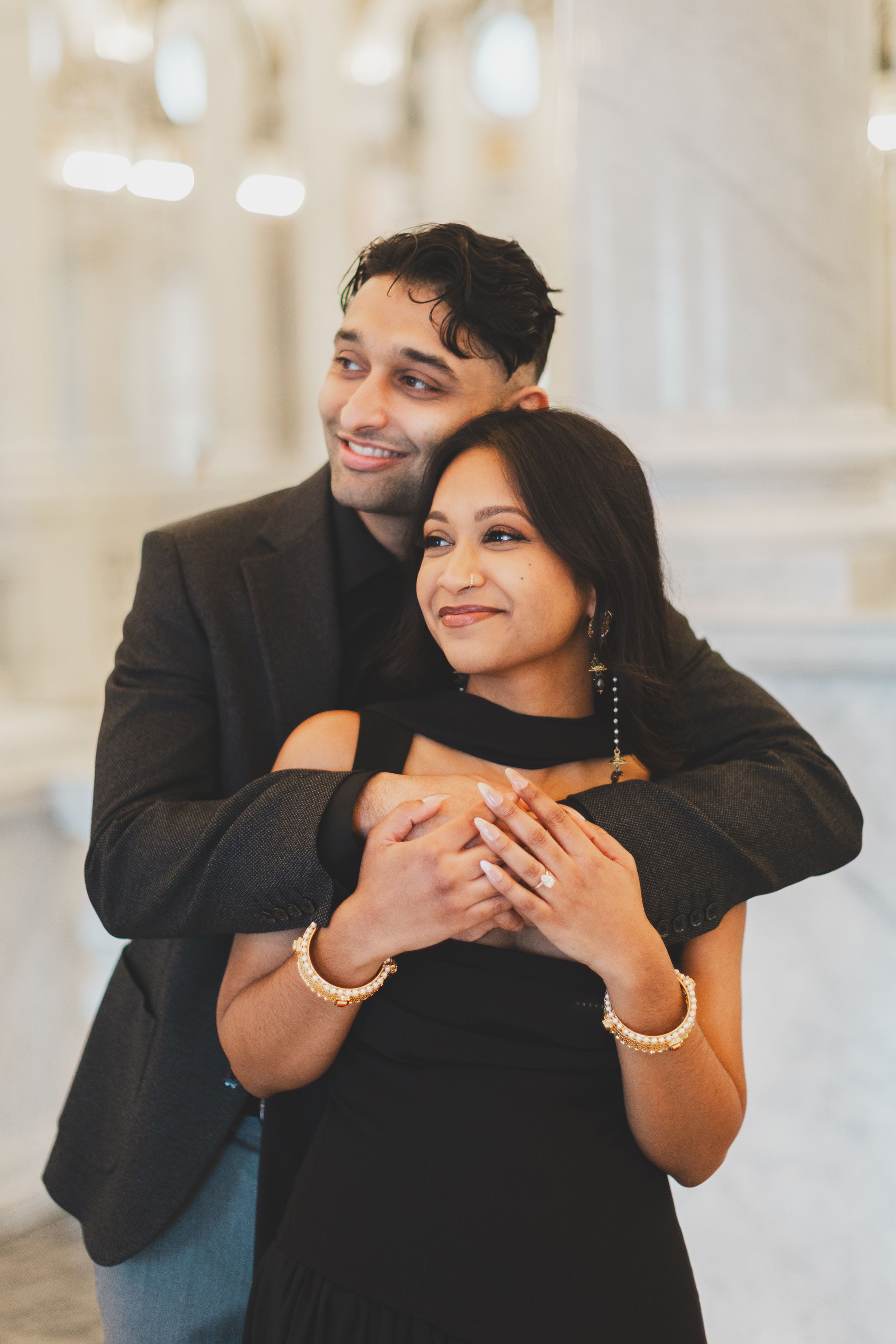 A couple embraces warmly in the library of congress engagement photoshoot, posing in an elegant marble interior.
