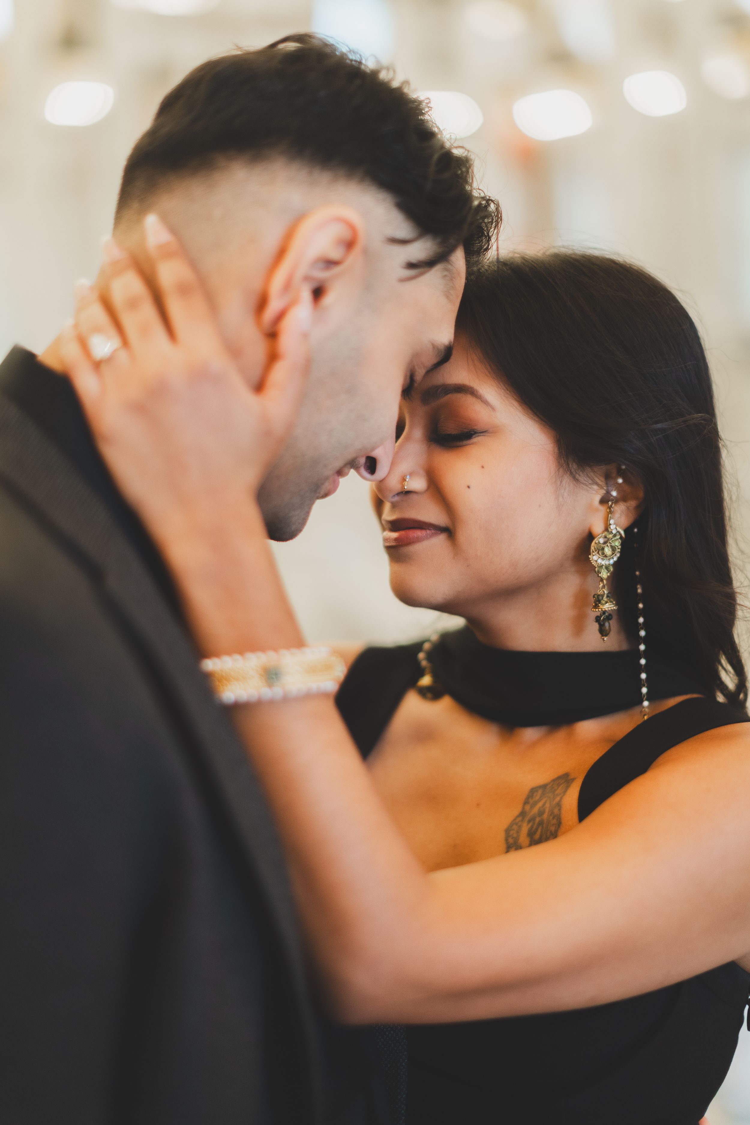 Couple sharing an intimate moment, foreheads touching, woman wearing gold earrings and black dress for their washington dc engagement shoot