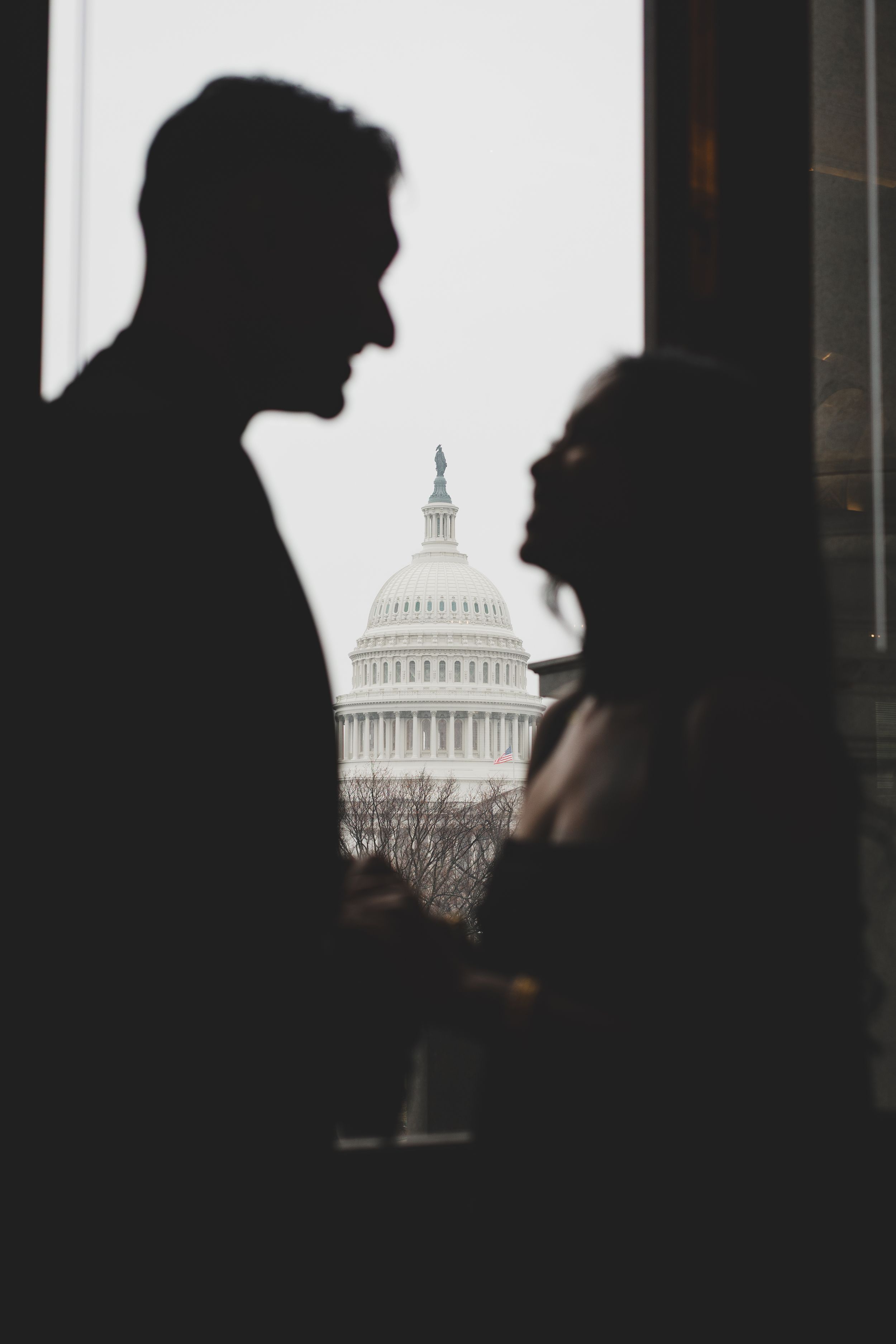 Silhouette of couple facing each other with U.S. Capitol Building dome visible in background.