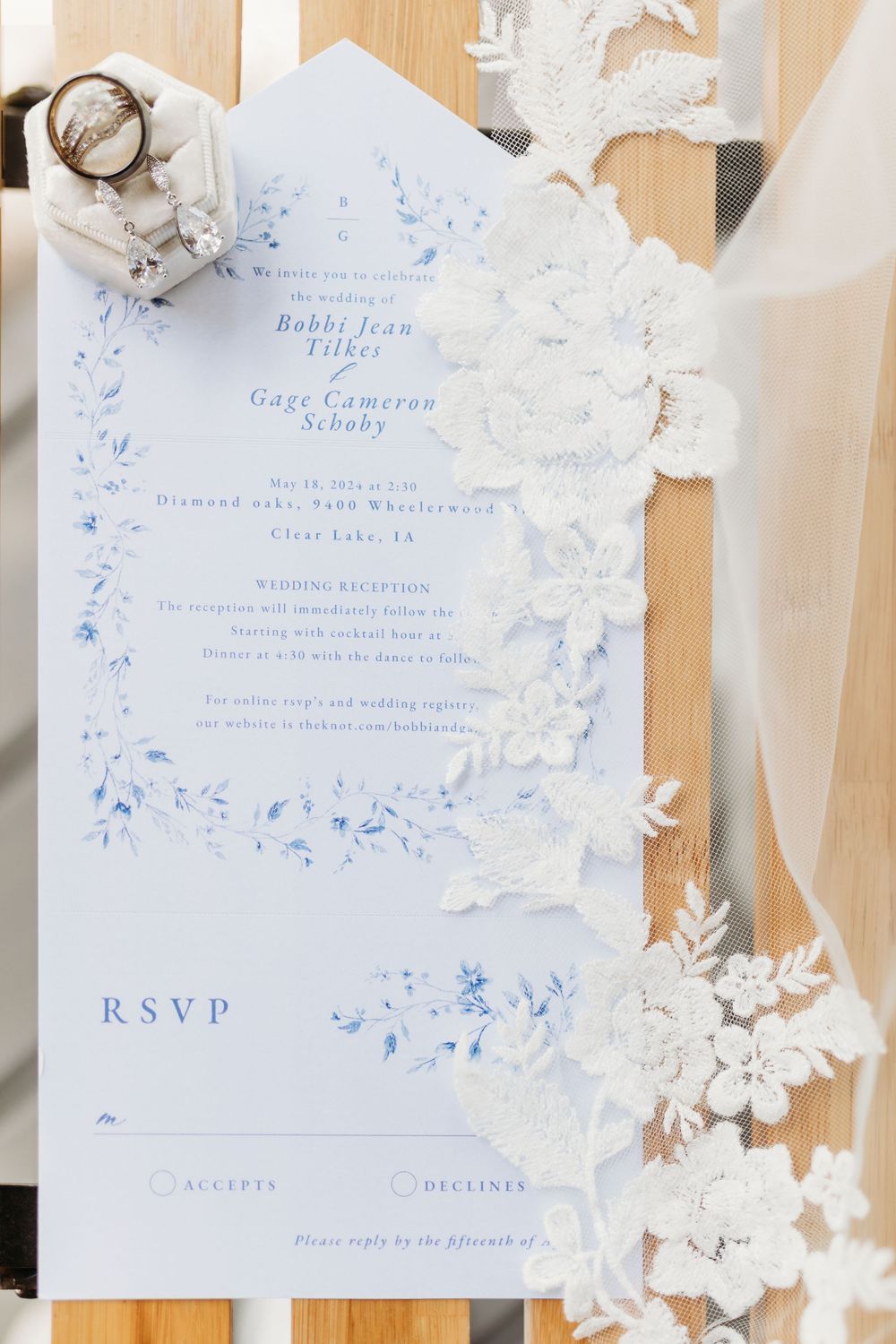 Blue floral wedding invitation suite with RSVP card and lace veil detail on wooden background.