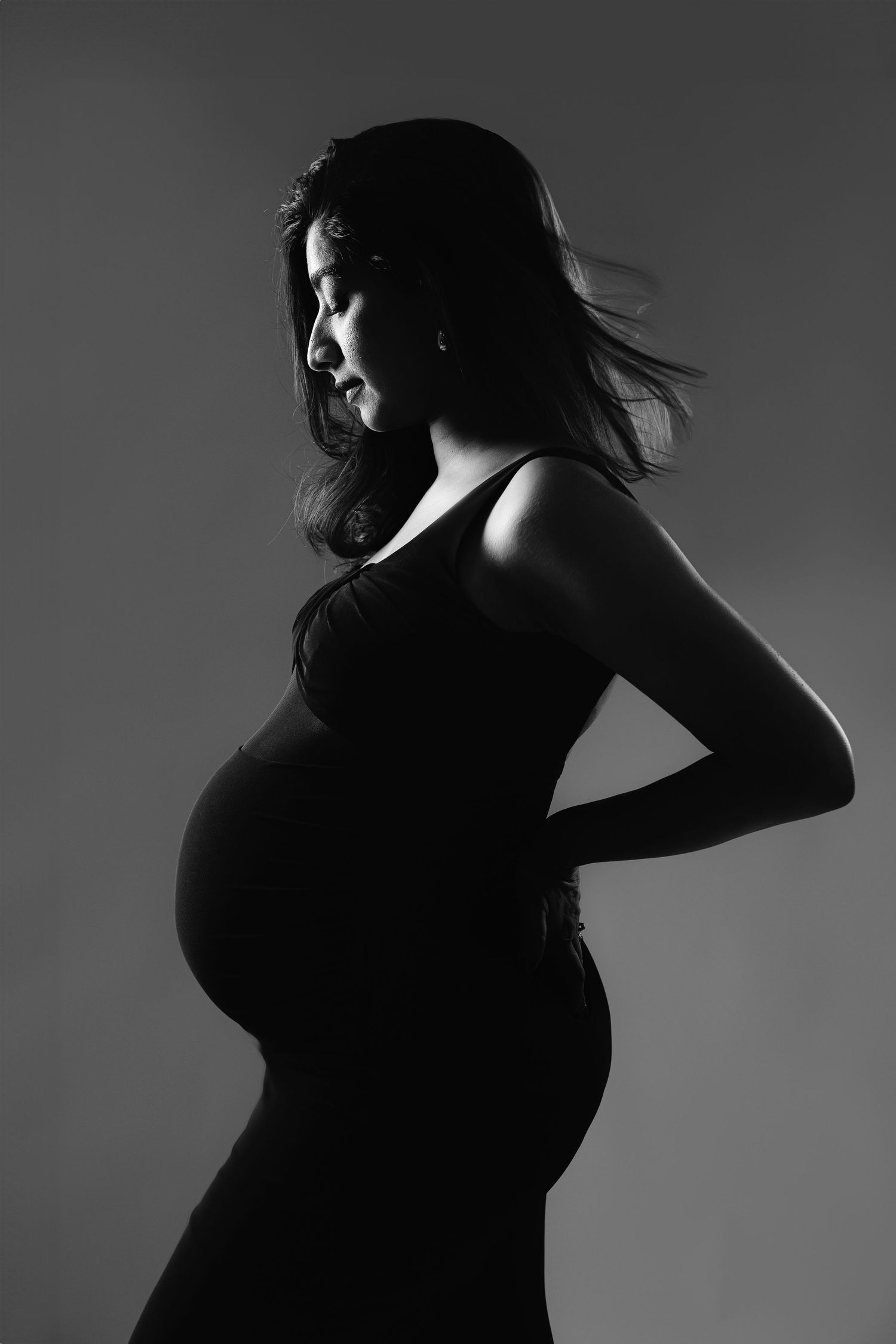 Black and white profile portrait of a pregnant woman in a sleeveless dress, showcasing her baby bump.