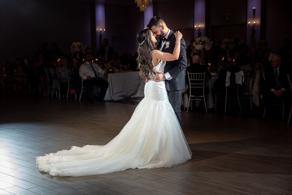 Bride and groom share intimate slow dance embrace in dimly lit romantic wedding ballroom.