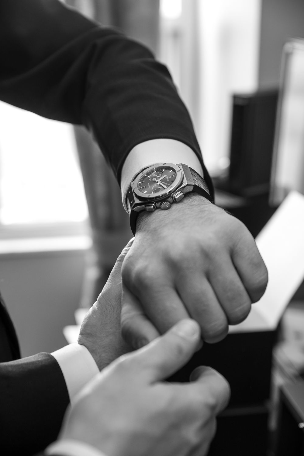 Black and white close-up of groomsman fastening a luxury watch on the grooms wrist before wedding.