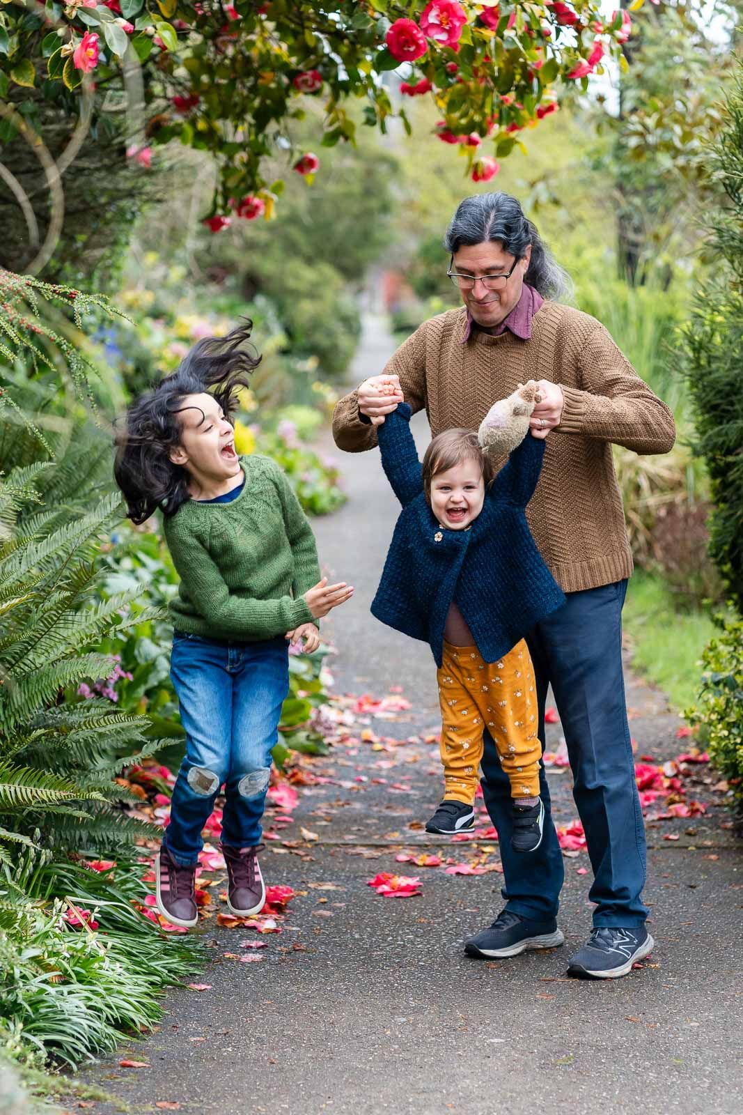 Dad swinging child while the other child jumps.
