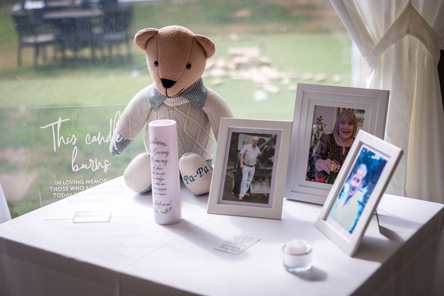 Sentimental wedding memory table featuring a teddy bear, candle, and framed photos of loved ones.