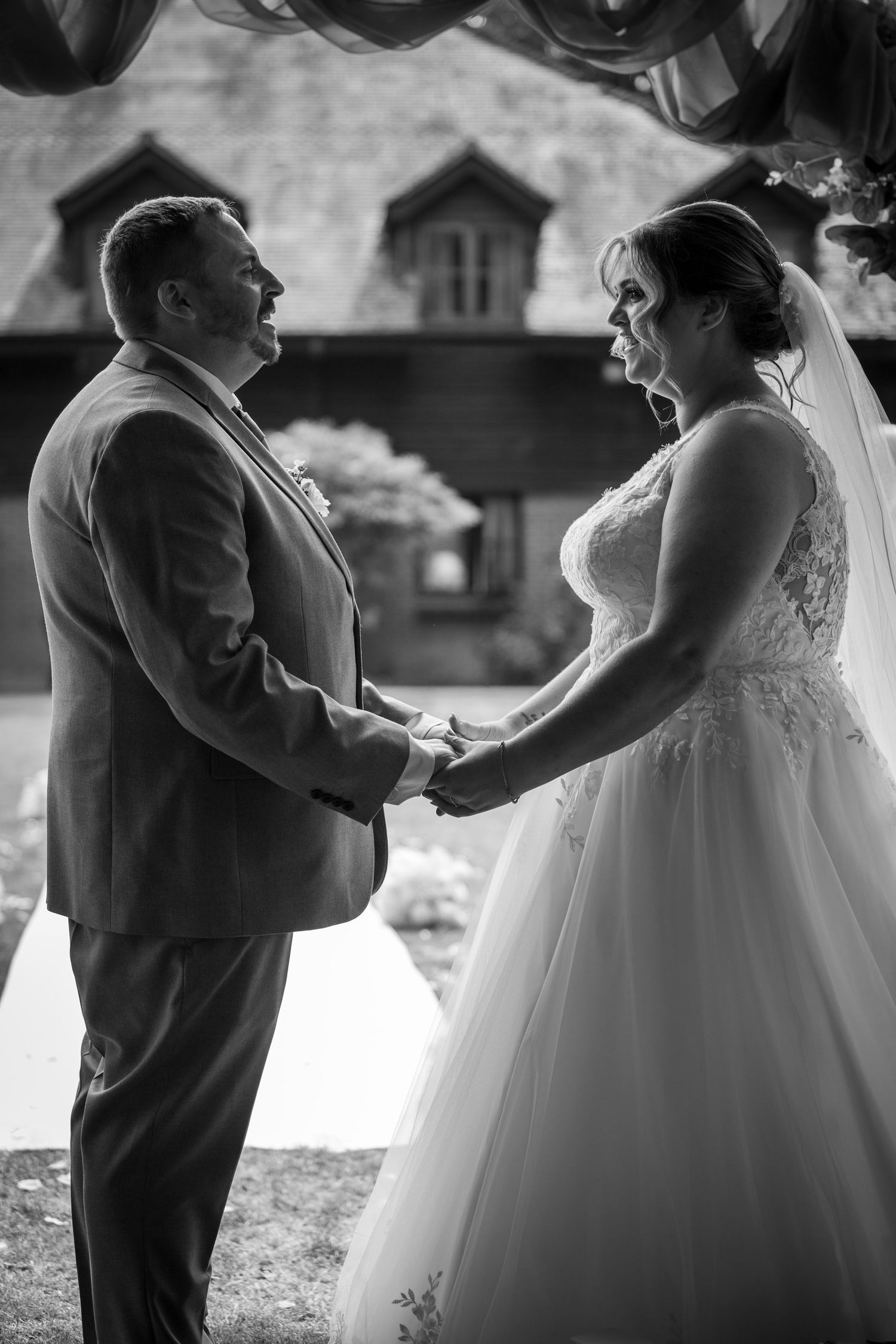 Black and white photo of bride and groom laughing while holding hands during their outdoor wedding ceremony.