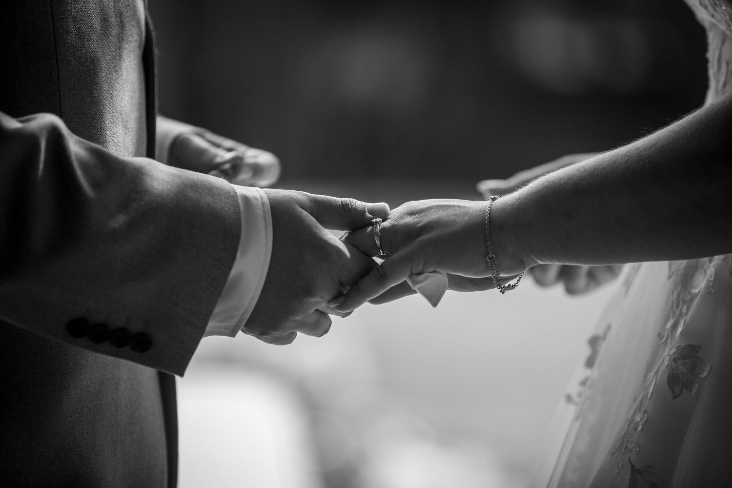 Close-up black and white photo of bride and groom holding hands tenderly during the wedding ceremony.