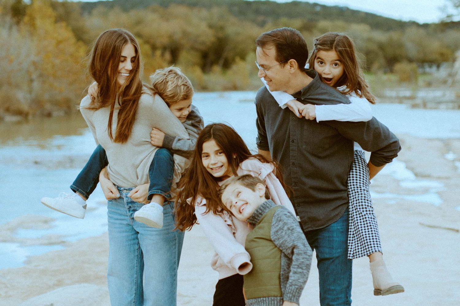 Parents giving piggyback rides to their children during a fun family photo shoot by the river in Wimberley, Texas.