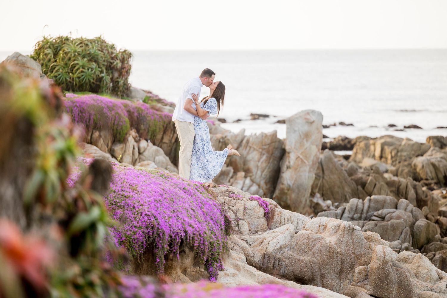 Couple embracing on a black sand beach with dramatic cliffs and turquoise waves in the background.