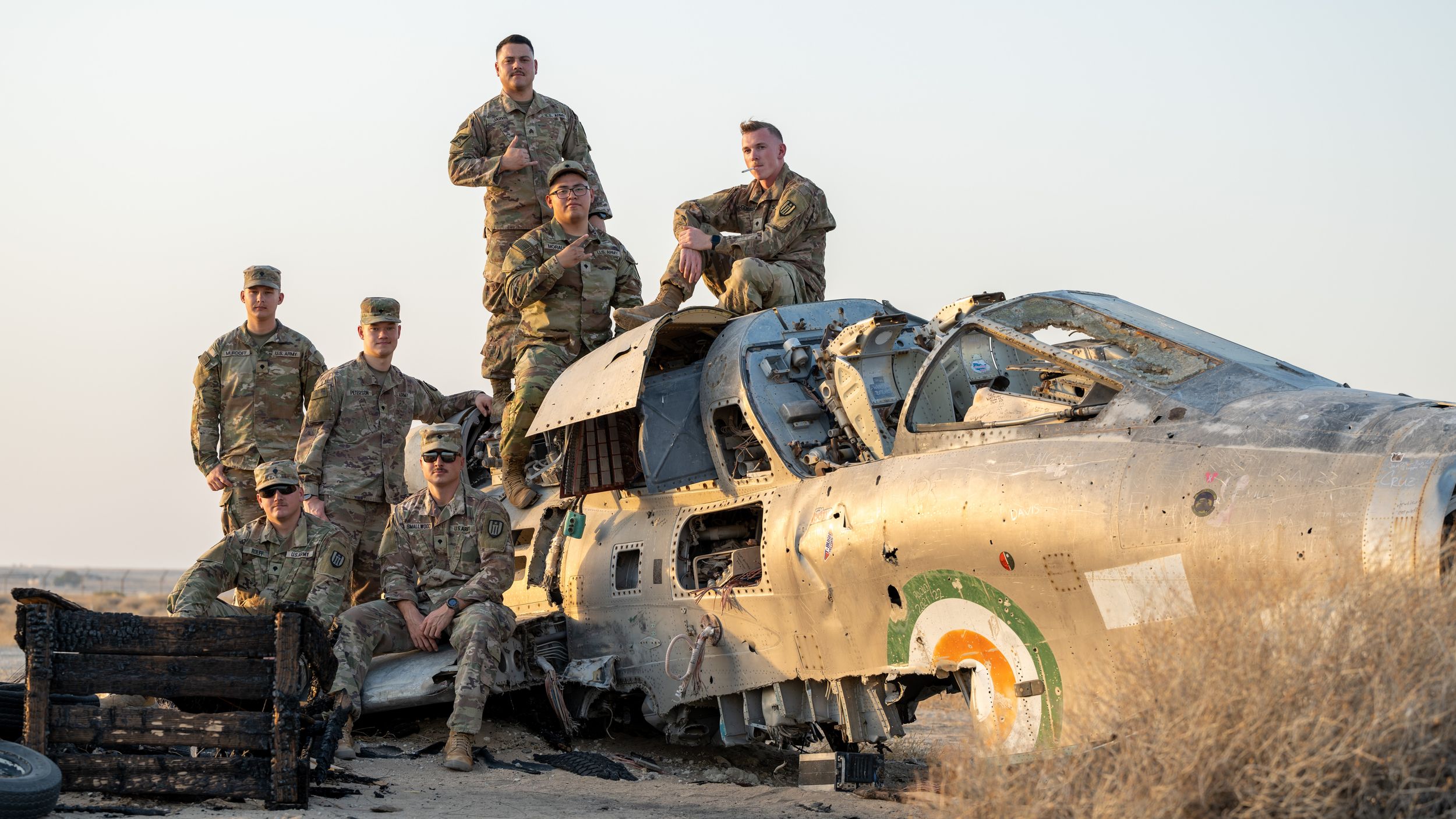 Military soldiers posing on a wrecked fighter jet aircraft in a desert landscape.