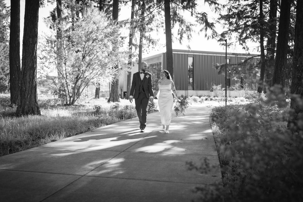 Black and white photo of bride and groom walking hand in hand on a pathway.