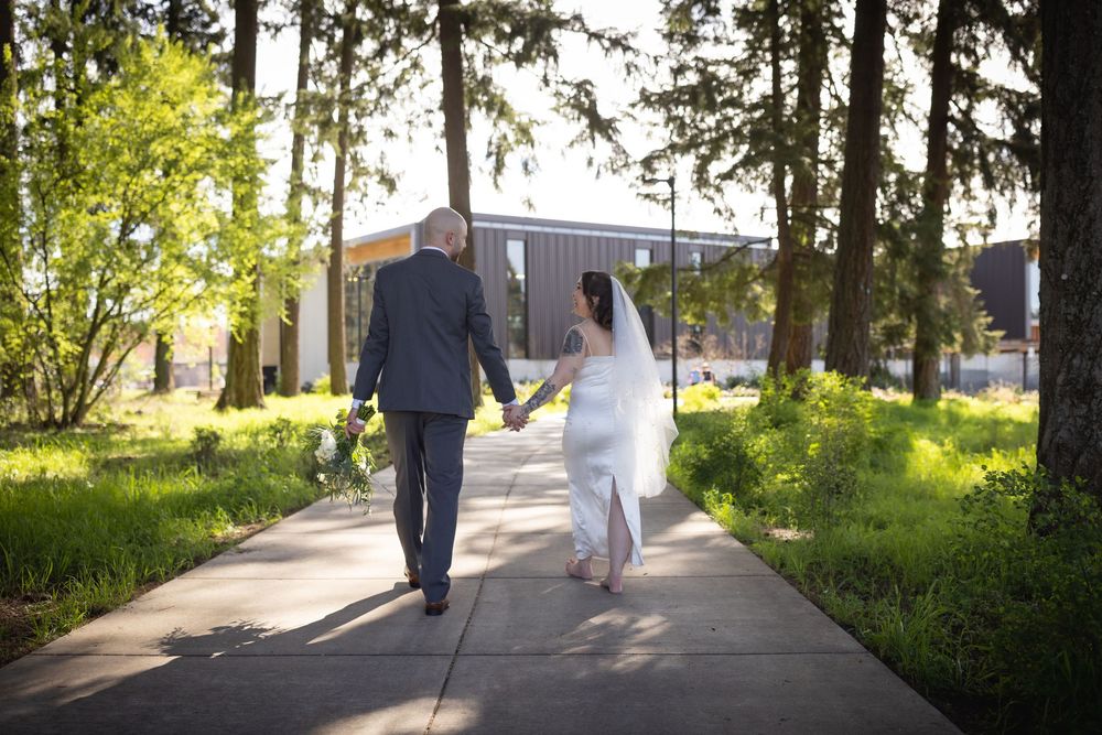 Bride and groom walk hand in hand down a sunlit tree-lined pathway.