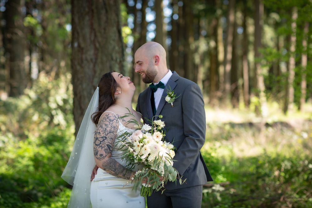 Bride and groom share a romantic moment smiling at each other in a pine forest.