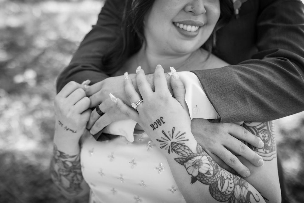 Black and white close-up of bride and groom hands showing tattoos and wedding rings.