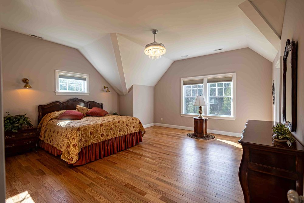 Spacious bedroom with vaulted ceilings, hardwood floors, a wooden bed frame, and two windows providing natural light.