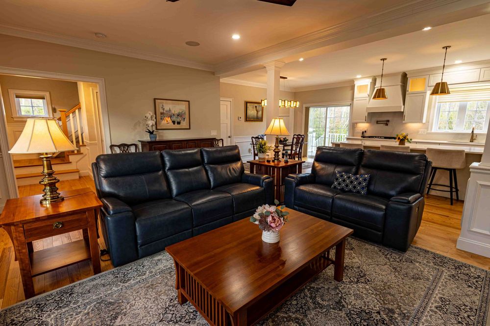 Spacious open-concept living room with navy leather sofas, hardwood floors, and views into a bright white kitchen.