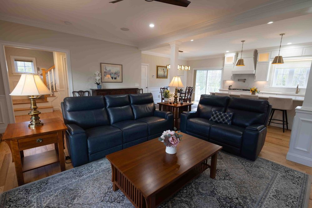 Open-concept living room with navy blue leather sofas, wood coffee table, and modern kitchen visible in background.