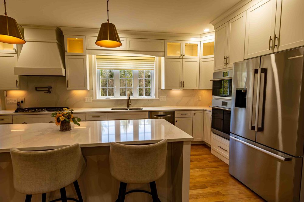 Modern kitchen with white cabinets, stainless steel appliances, quartz island, pendant lights, and hardwood floors.