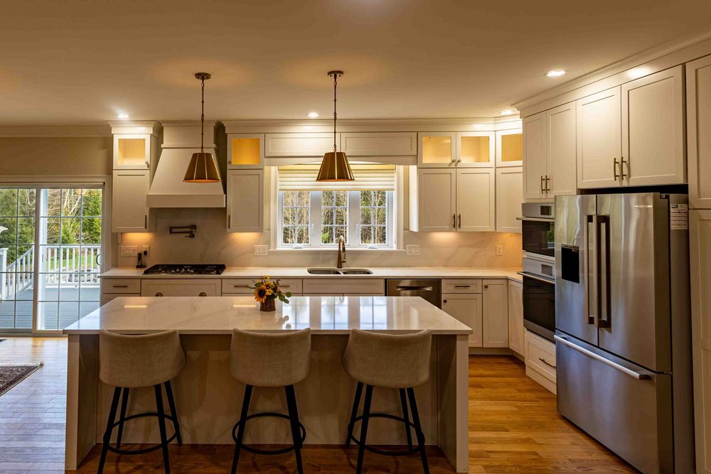 Modern white kitchen with island seating, pendant lights, stainless steel appliances, and hardwood floors.