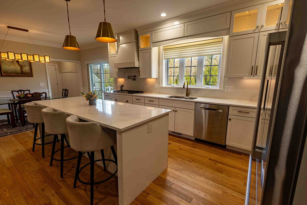 Modern kitchen with white island, gray cabinets, pendant lights, and stainless steel appliances on hardwood floors.