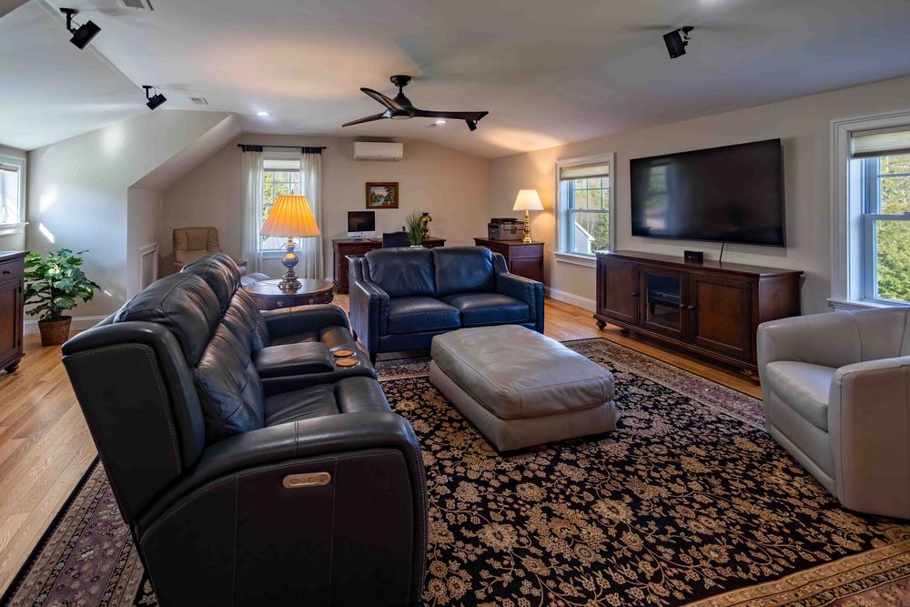 Spacious living room with leather recliners, dark wood TV console, fireplace, and ornate area rug on hardwood floors.