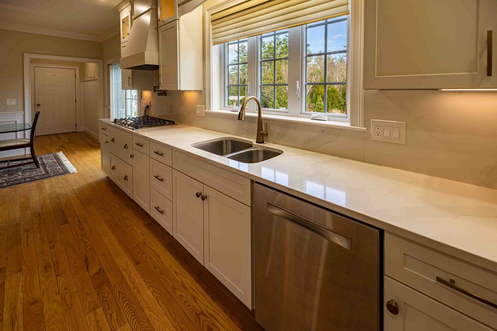 Modern kitchen with white shaker cabinets, quartz countertops, stainless steel sink, and hardwood floors.