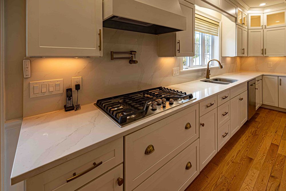 Modern white kitchen with marble countertops, gas stovetop, custom cabinetry, pot filler faucet, and hardwood floors.