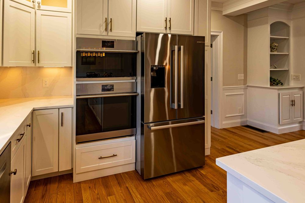 Modern kitchen with stainless steel French door refrigerator, double wall oven, and white shaker cabinets with hardwood floors.