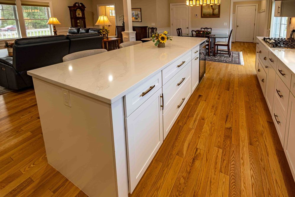 Large white kitchen island with quartz countertop and shaker cabinets on warm hardwood floors.