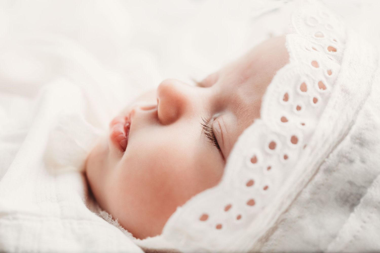 Black and white photo of smiling parents tenderly holding their swaddled newborn baby together.