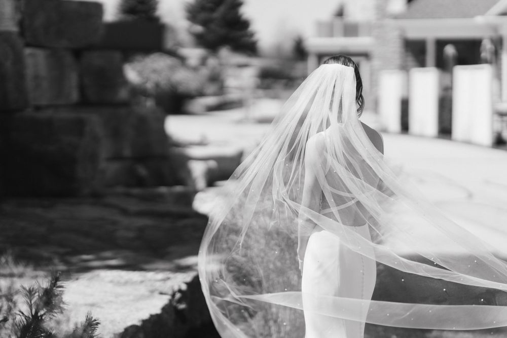 Black and white photo of a bride in a flowing veil and wedding gown outdoors near stone landscaping.