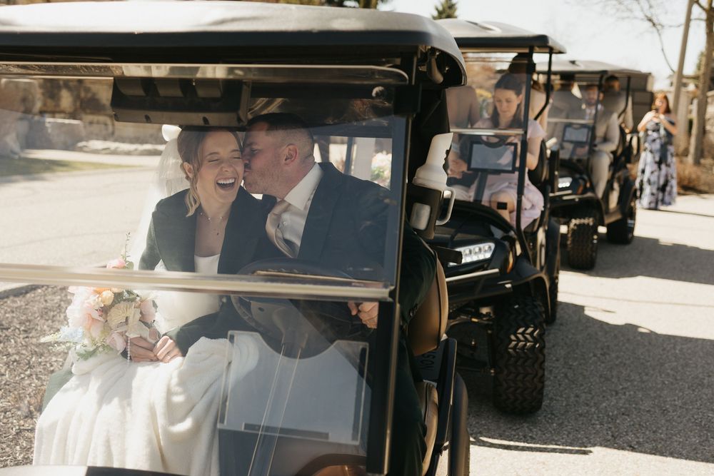 Bride and groom laughing together in a black golf cart during their wedding day transportation.