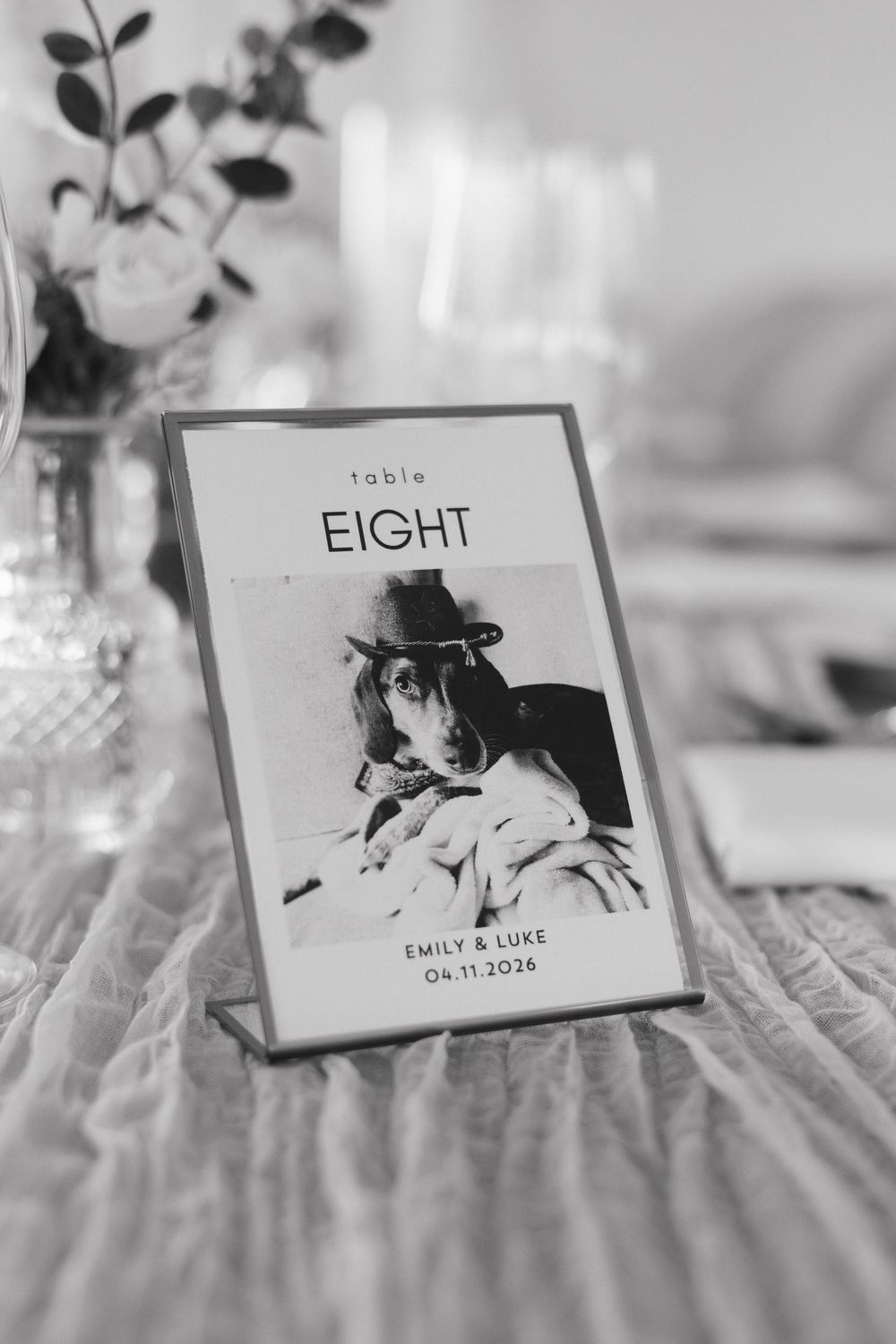 Black and white wedding table number eight card featuring a dog photo, personalized for Emily and Luke, April 11, 2026.