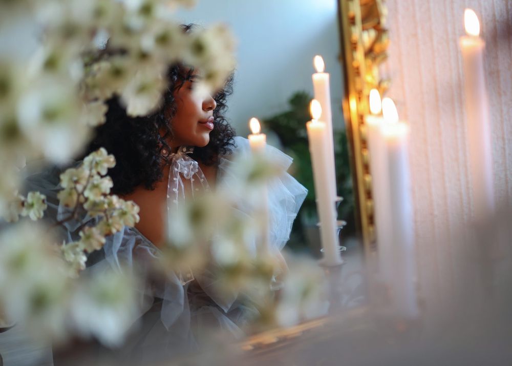 Elegant bride surrounded by white candles and floral arrangements in a dreamy, softly lit wedding setting.