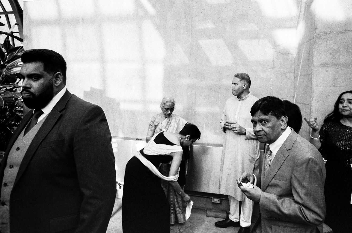 Black and white photo of elegantly dressed guests gathered at an indoor multicultural wedding ceremony.
