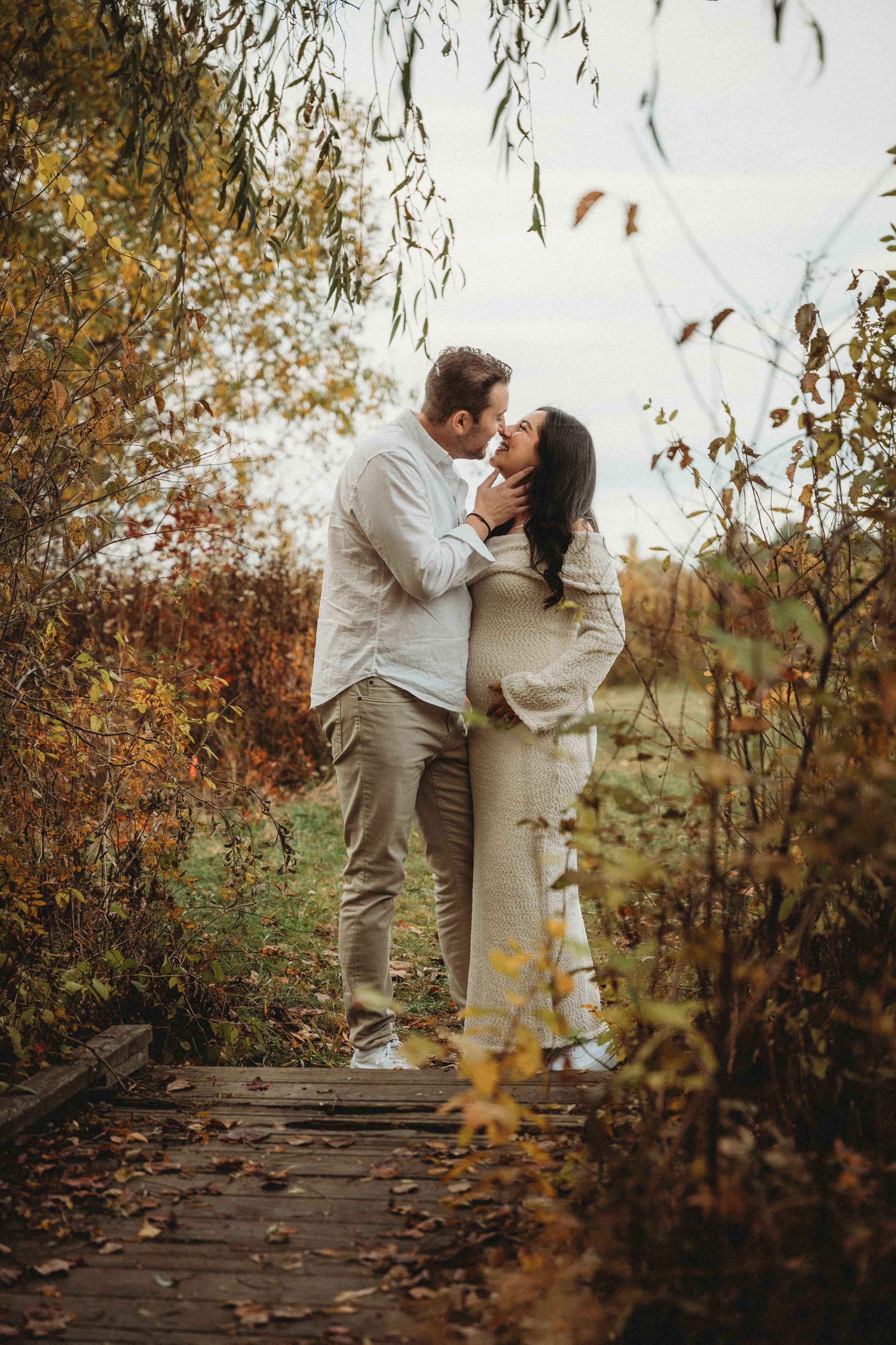 Couple sharing a romantic kiss on a wooden path surrounded by colorful autumn foliage.
