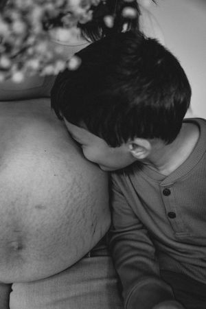 Black and white photo of a young boy kissing his mother's pregnant belly in a tender maternity moment.