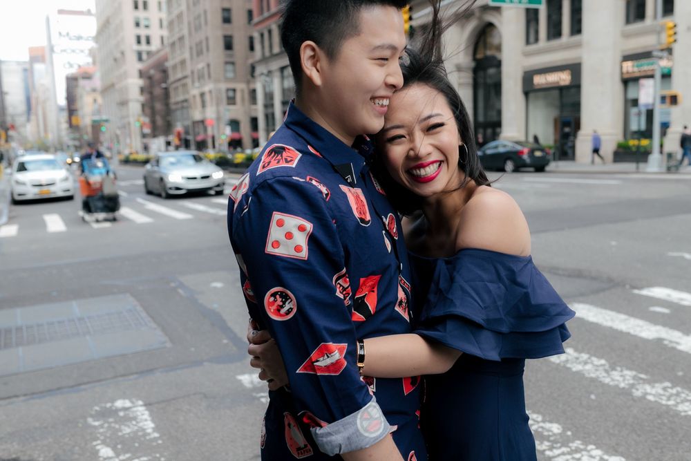 Couple embracing and smiling on a city street corner, wearing coordinating navy blue outfits in an urban setting.