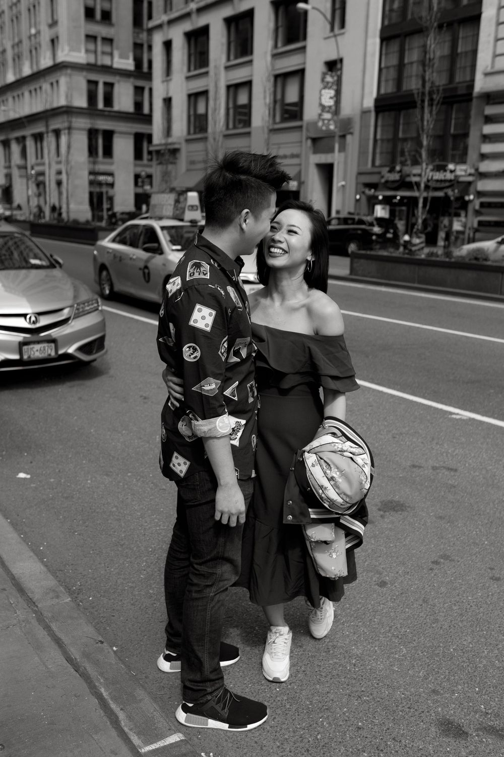 Black and white photo of a couple sharing a romantic moment on a city street, with taxis and buildings in the background.