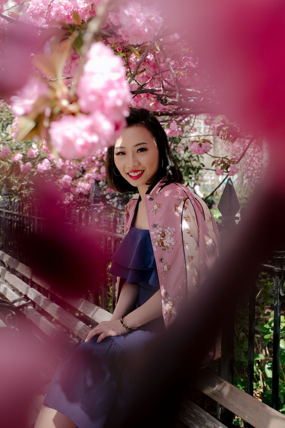 Woman smiling surrounded by vibrant pink cherry blossoms in full bloom outdoors.